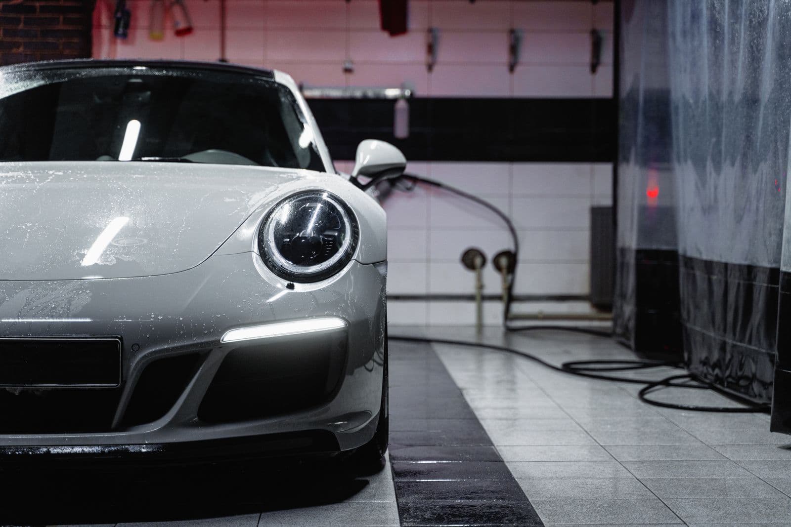 Wet Porsche in a tiled detailing bay with water beading across the hood and headlights on.