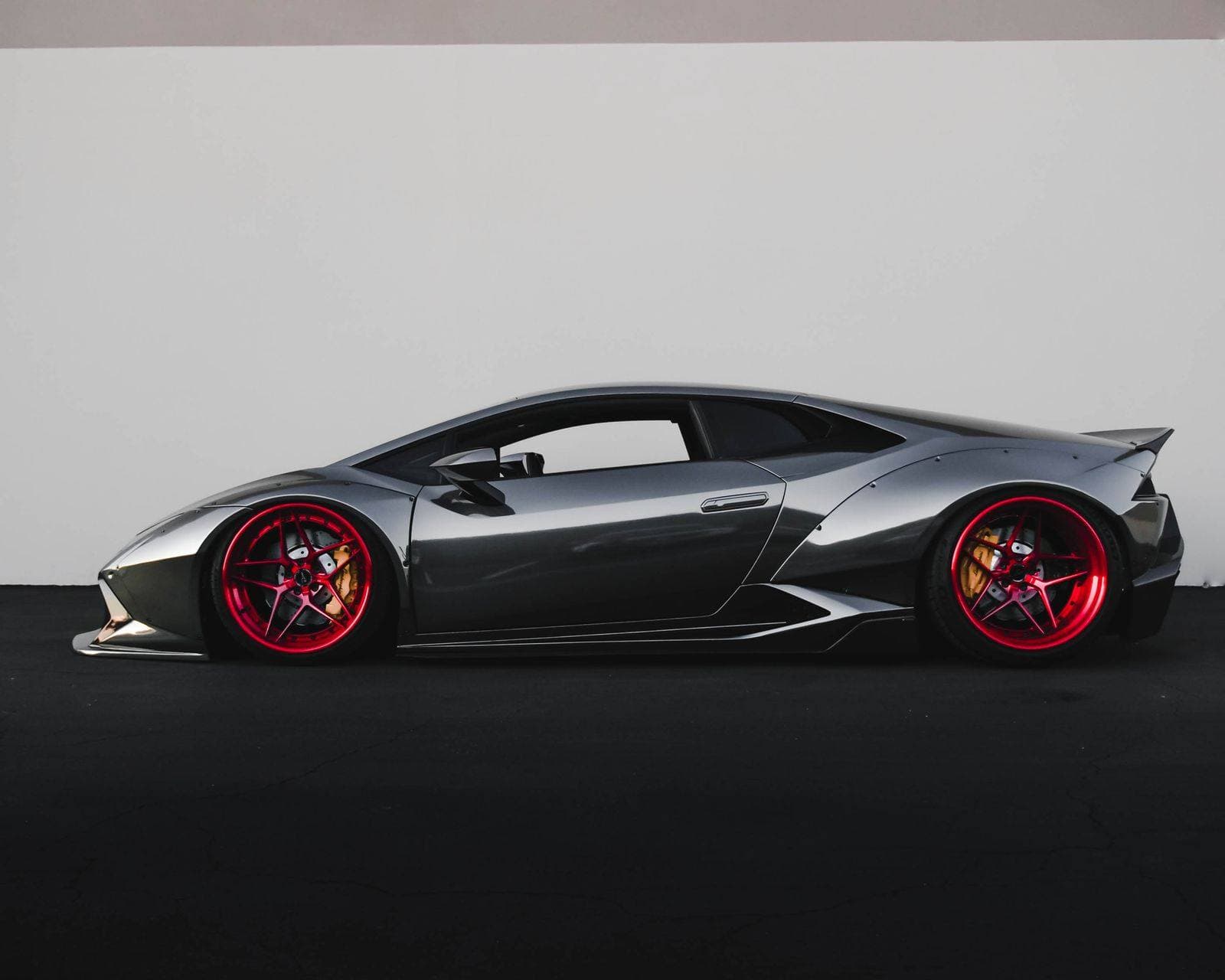 Grey sports coupe with red wheels parked against a plain wall, shown as a finished paint surface.