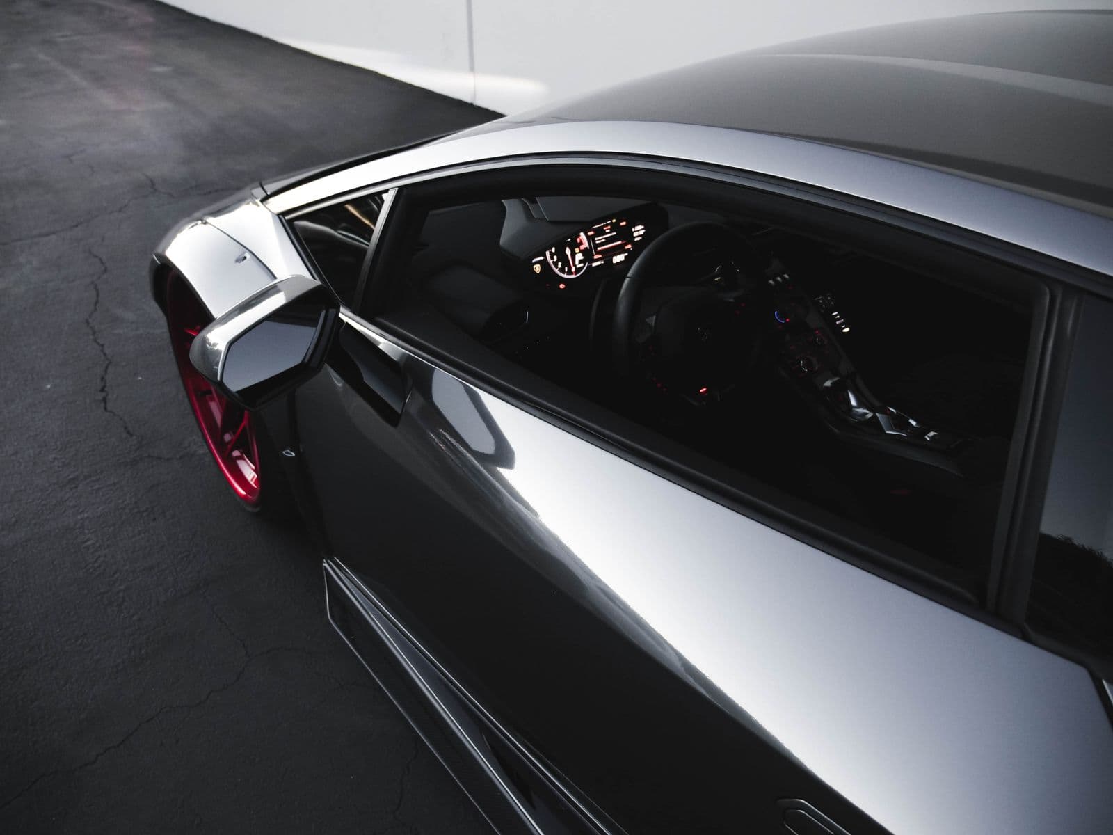 Charcoal luxury sports-car cabin seen from above, with digital gauges and a red alloy wheel.