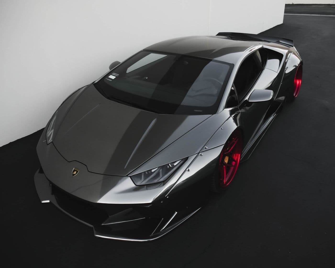 Charcoal Lamborghini with a high-gloss paint finish and metallic red multi-spoke wheels.