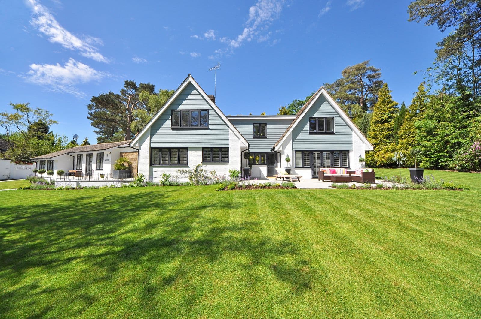 White-brick home with a striped lawn, stone patio seating, and established planting.