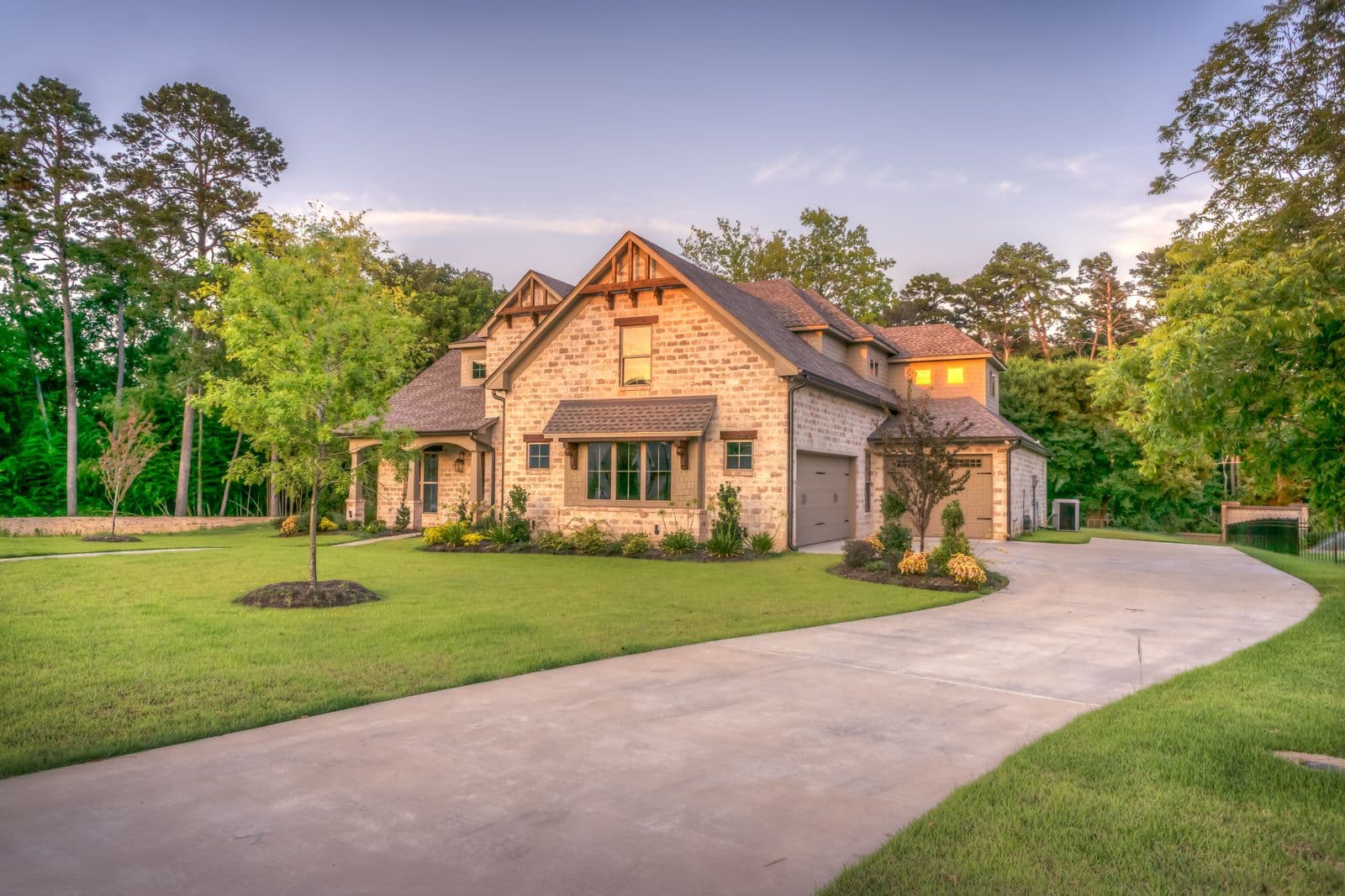 Stone-and-brick home at golden hour with a curved concrete driveway and landscaped lawn.