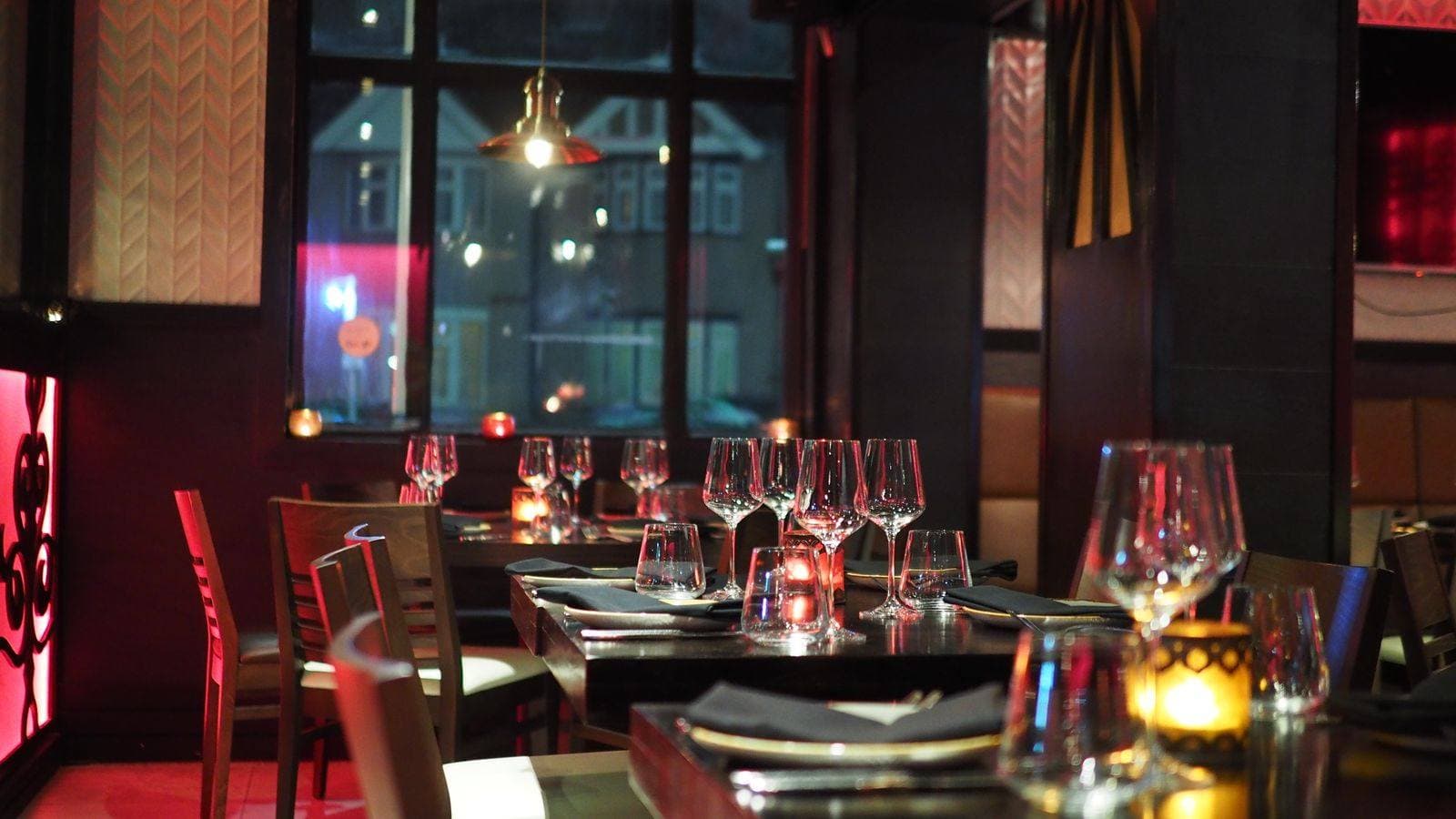 Evening dining room with dark tables, wine glasses, black napkins, and candlelight.